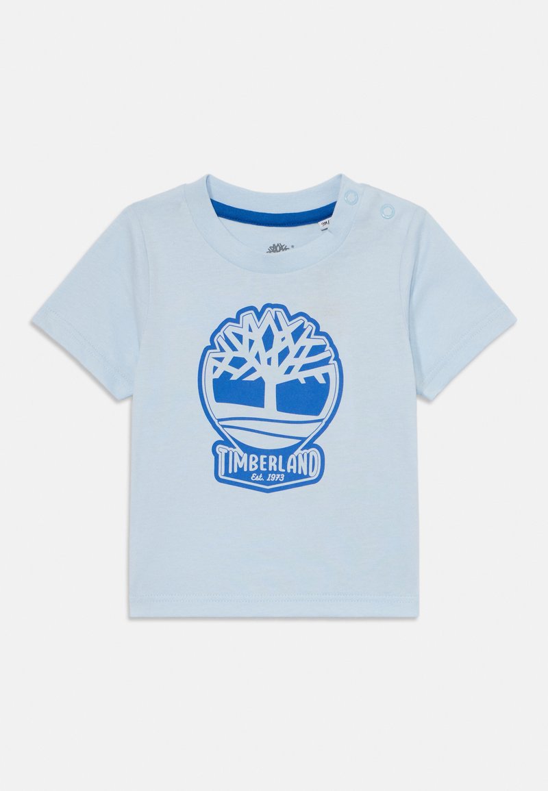 Šviesiai mėlyna trumpomis rankovėmis T-marškiniai, pagaminti iš medvilnės, su mėlynu medžio logotipu ir užrašu "Timberland Est. 1973" centre. Su spaustuku prie pečių.