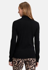 Fekete kötött pulóver magas gallérral és bordázott mandzsettával, állatmintás leggingsekkel párosítva. Puha tapintás és testhezálló dizájn.