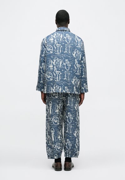 Σετ από τζιν ζακέτα και παντελόνι με λευκά αφηρημένα σχέδια σε μπλε φόντο. Χαλαρή εφαρμογή με υφή και σχεδιασμό με φαρδιά μπατζάκια.