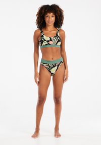 Čierne bikiny s tropickým vzorom zelených listov, ktoré majú športový dizajn. Vrchná časť má široké ramienka a kontrastný zelený pás na spodnej časti.