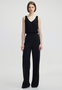 Černý bezramenný top s výst řihem do V v kombinaci s volnými černými kalhotami. Hladká textura, minimální design a rovný střih.