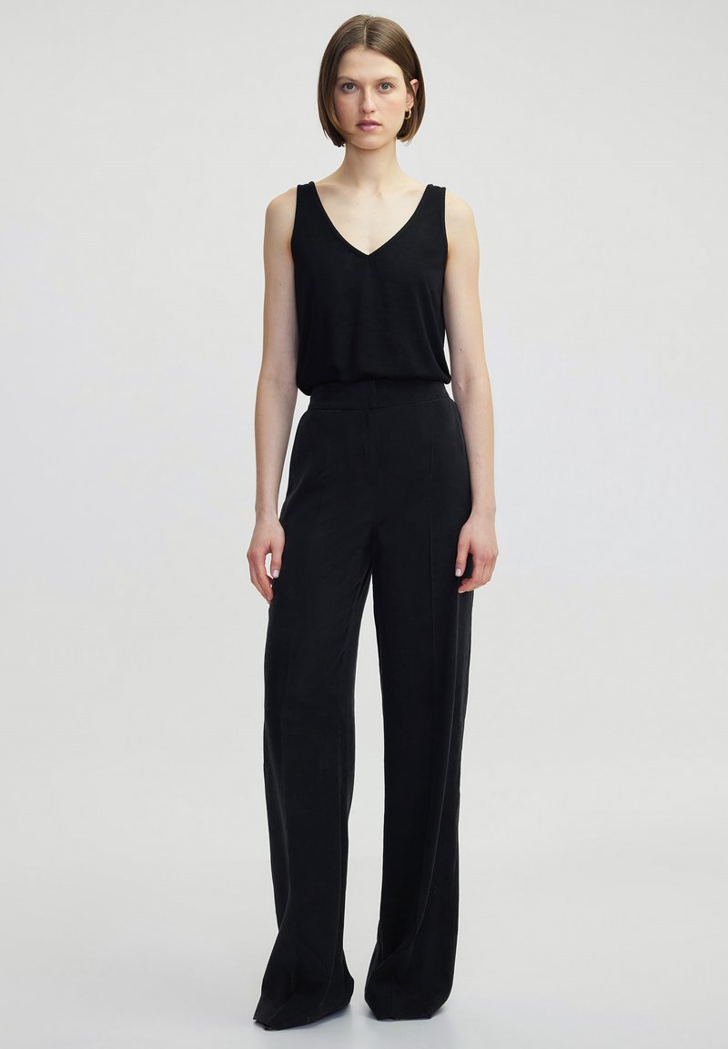 Černý bezramenný top s výstřihem do V v kombinaci s volnými černými kalhotami. Hladká textura, minimální design a rovný střih.