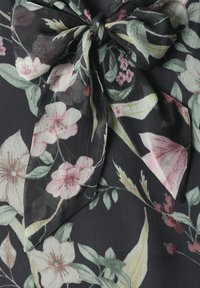 Tissu noir avec un grand nœud noué présentant un motif floral de fleurs roses et blanches avec des feuilles vertes.