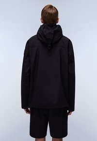Giacca nera con cappuccio, dal taglio rilassato, dotata di un toggle al collo e tasche laterali, abbinata a pantaloni corti neri. Texture morbida.