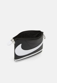 Čierny a biely zipsový obal vyrobený z syntetického materiálu, s výrazným bielym logom Nike a elegantným zaobleným dizajnom.
