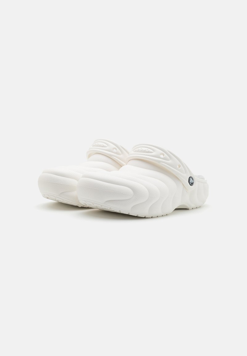 Par de zuecos blancos sin cierre con patrón de olas texturizado y correas de talón ajustables, mostrados sobre un fondo blanco liso.