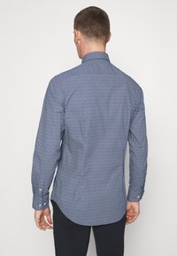 Tummansininen pitkähihainen paita, jossa on geometrinen kuvio. Valmistettu sileästä kankaasta, siinä on istuva malli, nappihihansuut ja kaareva helma.