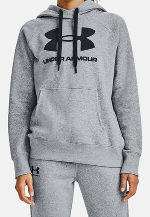 Persoon draagt een grijze Under Armour hoodie met zwart logo en bijpassende grijze joggingbroek, waarbij een deel van de handen en torso zichtbaar is.