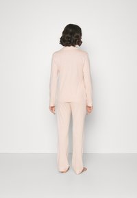 Hellrosa Schlafanzug-Set mit vertikalen Streifen; langärmliges Oberteil mit weichem Material und passende Hose mit lässiger Passform.