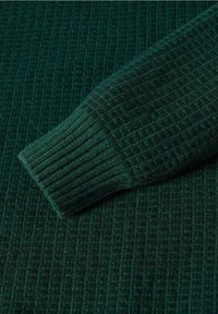 Manche de pull en maille vert foncé avec une texture côtelée et de subtils motifs carrés. Matière douce et design de poignet effilé.