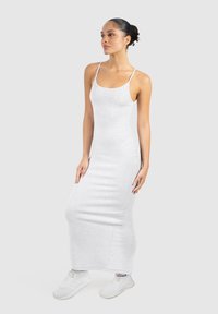 Largo vestido de algodón blanco con tirantes finos, silueta ajustada y dobladillo a la altura de la rodilla. Llevado con zapatillas deportivas blancas. Textura suave.