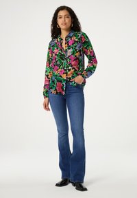 Multicolore bloemenblouse met groene, roze, oranje en blauwe tinten. Gecombineerd met een aansluitende blauwe flared jeans en zwarte enkellaarsjes.