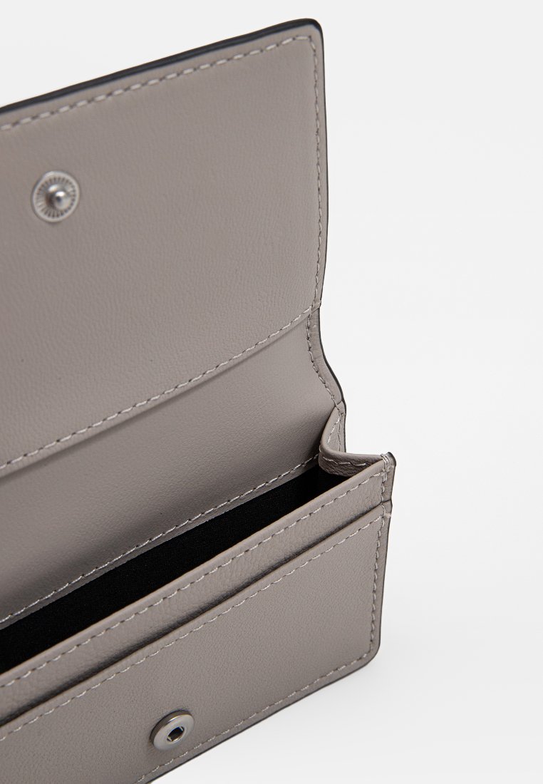 Grauer Ledergeldbeutel geöffnet, der das leere Hauptfach mit silbernem Druckknopfverschluss vor einem weißen Hintergrund zeigt.