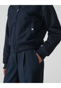 Marine Bomberjacke mit gerippten Bündchen und Saum; verfügt über einen silbernen Reißverschluss und eine Seitentasche mit Druckknopf.