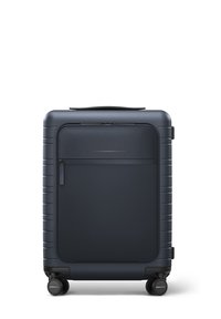 Valise rigide bleu marine avec une texture lisse, dotée d'une poche zippée à l'avant, d'une poignée supérieure et de quatre roues pour une mobilité aisée.