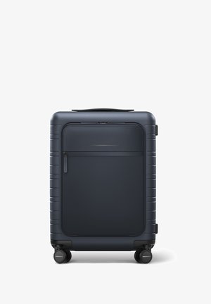 Valise rigide bleu marine avec une texture lisse, dotée d'une poche zippée à l'avant, d'une poignée supérieure et de quatre roues pour une mobilité aisée.