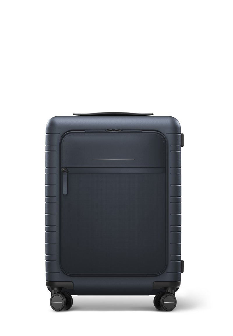 Valise rigide bleu marine avec une texture lisse, dotée d'une poche zippée à l'avant, d'une poignée supérieure et de quatre roues pour une mobilité aisée.