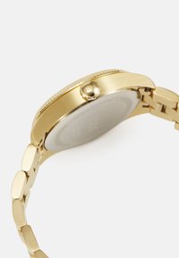 Montre-bracelet dorée avec un boîtier rond, une couronne texturée et un bracelet à maillons. Acier inoxydable, étanche, design minimaliste.