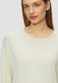 Lichtbeige oversized lange mouw top met een ronde halslijn en een zachte textuur, met verlaagde schouders en minimale naden.
