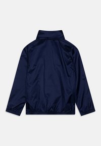 Veste coupe-vent bleu marine avec un col montant, des poignets élastiques et une texture lisse et légère. Design épuré, sans fermetures visibles.