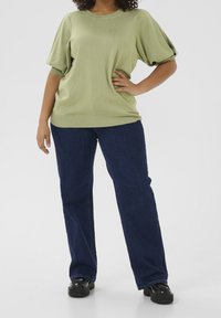 Lichtgroene top met textuur en pofmouwen, gecombineerd met donkerblauwe jeans met rechte pijpen en zwarte platformschoenen. Eenvoudig, casual ontwerp.