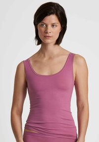 Fitted pink tank top with wide straps, made from a smooth, soft fabric. Features a rounded neckline and a seamless design at the hem.