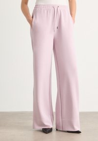 Light pink wide-leg sweatpants made of soft material, featuring an elastic waistband with drawstring and side pockets.