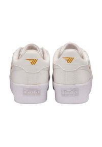 Vita lädersneakers med låg silhuett, med en texturerad vit gummisula och gyllene detaljer på hälen och logotypen.