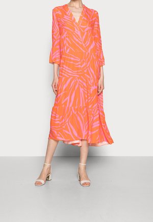 Vrouw die een oranje jurk van middellange lengte draagt met roze zebraprinten en driekwart mouwen, gecombineerd met witte enkellaarzen met blokhakken en enkelbandjes.