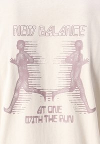 Kremna majica s rozastim grafikom dveh tekačev in besedilom "NEW BALANCE AT ONE WITH THE RUN" pod njimi.