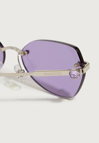 Akiniai nuo saulės su purpurine tonacija, juodais gradientiniais kraštais ir sidabro metaliniu rėmu. Rėmas papuoštas Swarovski kristalu ant šventyklos.