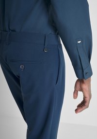 Pantaloni blu navy con una texture liscia, tasca laterale, tasca posteriore con bottone e cintura regolabile elegante con fibbia metallica.