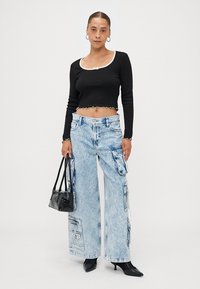 Black cropped top with cream trim, light blue wide-leg cargo jeans featuring pockets, paired with a small black handbag and heeled shoes.