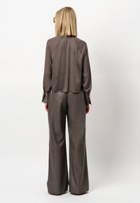 Bruine satijnen top met lange mouwen, gecombineerd met hooggerichte, wijde bruine leren broek. Beide stukken hebben een ontspannen pasvorm en minimale details.