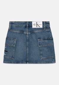Džínová sukně ve středně modrém odstínu, s dvěma velkými předními kapsami a bílou štítkem s logem „Calvin Klein Jeans“ na zadní straně.