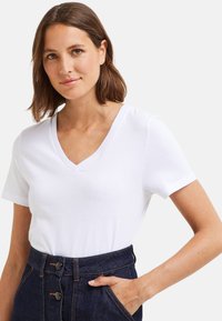 T-shirt blanc à col en V en coton. Manches courtes, texture lisse, associé à un pantalon en denim foncé taille haute avec des détails de boutons.