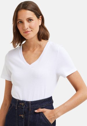T-shirt blanc à col en V en coton. Manches courtes, texture lisse, associé à un pantalon en denim foncé taille haute avec des détails de boutons.