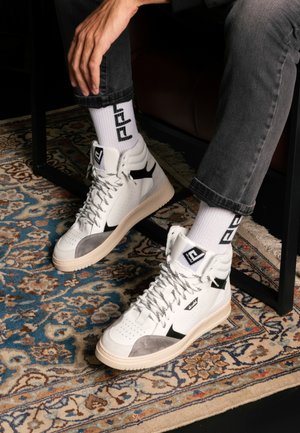 Le sneaker alte presentano una tomaia in pelle bianca con accenti in suede grigi e dettagli neri. Suola testurizzata e calzini bianchi a fantasia visibili.