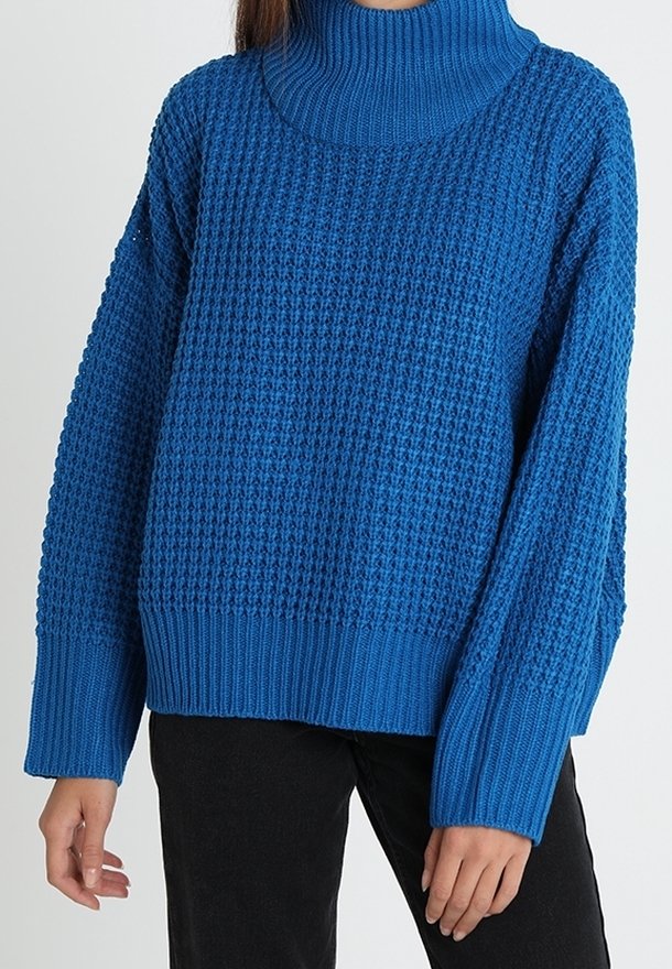 Pull en maille bleu avec un col montant côtelé et des manches larges et amples. Motif texturé avec un ourlet côtelé uni en bas.