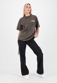 Donkergrijs oversized t-shirt met een vervaagde textuur, gecombineerd met losse zwarte cargo-broeken met zijzakken en ritsen, gedragen met witte sneakers.