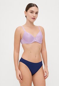 Lila podložna modrček z čipkastim obrobljenjem in nastavljivimi naramnicami, v kombinaciji z mornarsko modrimi brezšivnimi bikini hlačkami, ki izpostavljajo gladko teksturo.
