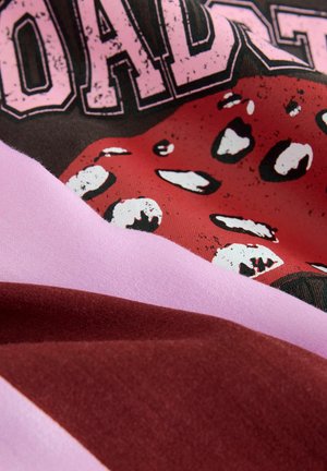 Grafischer Druckstoff mit einem roten Zungenmotiv auf schwarzem Hintergrund, kombiniert mit pinken und burgunderfarbenen Stoffabschnitten. Weiche Textur.