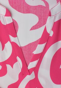 Primo piano di tessuto rosa e bianco con motivo astratto e dettaglio della cucitura a V sullo scollo.