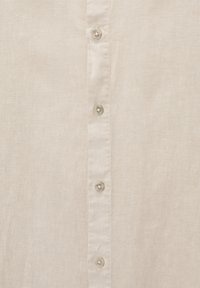Section de chemise en lin beige avec une rangée verticale de quatre boutons translucides et des coutures visibles le long de la patte de boutonnage.