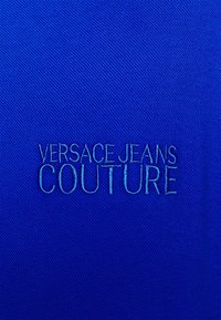 Modrý látkový materiál s vyraženým logem: "VERSACE JEANS COUTURE" ve stříbrné nitě, s hladkým povrchem a jemnými detaily.