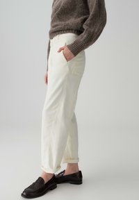 Pantaloni di jeans bianchi, dal taglio morbido e ampio, con grandi tasche, orli risvoltati e cuciture tonali, abbinati a mocassini scuri e un maglione grigio a maglia.