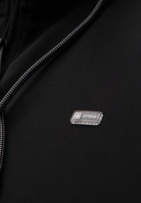 Gros plan d’un tissu noir avec un cordon gris et blanc et une petite étiquette transparente portant la mention « ombre » sur la surface.
