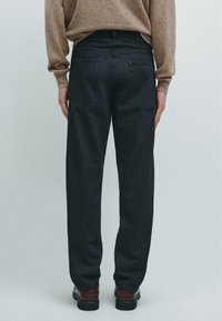Tmavě modré džíny s volným střihem, s dvěma zadními kapsami a jednoduchým designem. Jako outfit je kombinováno s béžovým svetrem a hnědými botami.