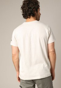 T-shirt beige clair à manches courtes en coton doux, avec un col rond et une finition texturée subtile sur le tissu.