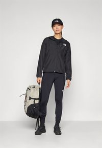 Črna lahka jakna, črne legice, črni supergi in črna kapa. Siva in črna nahrbtnik z nastavljivimi trakovi, nošen na strani.